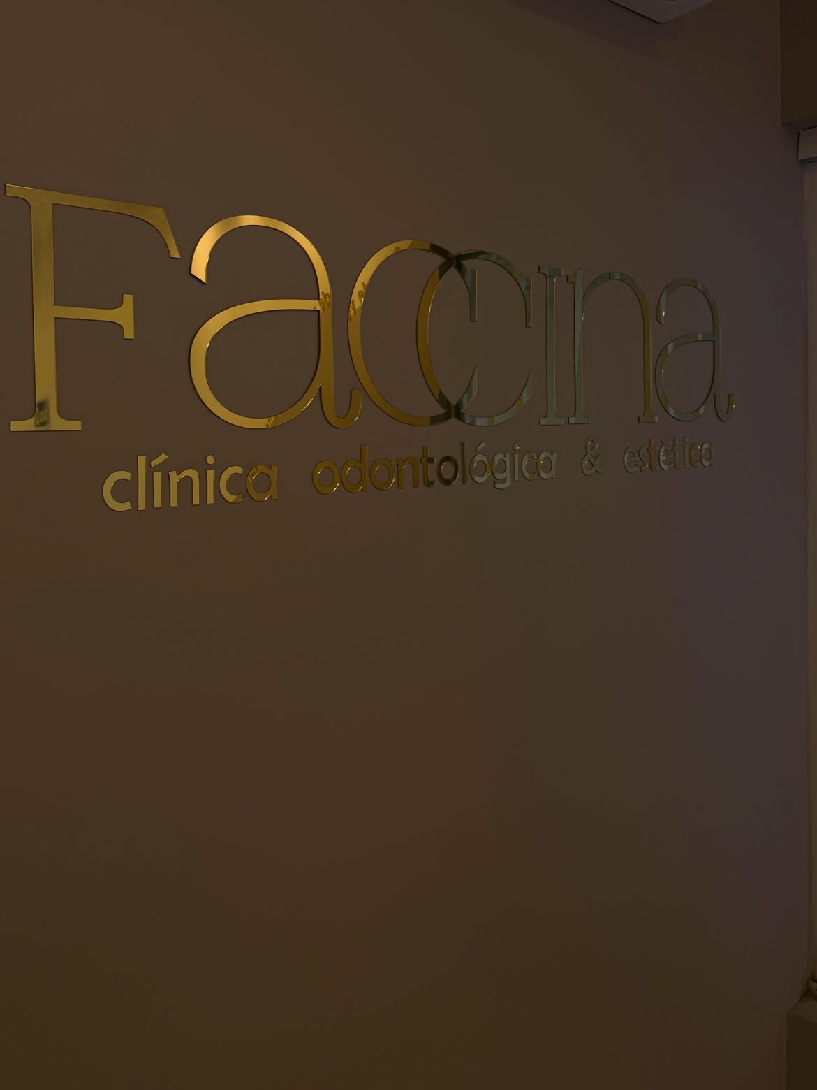 Letreiro dourado da Faccina na parede, com “clínica odontológica & estética” embaixo