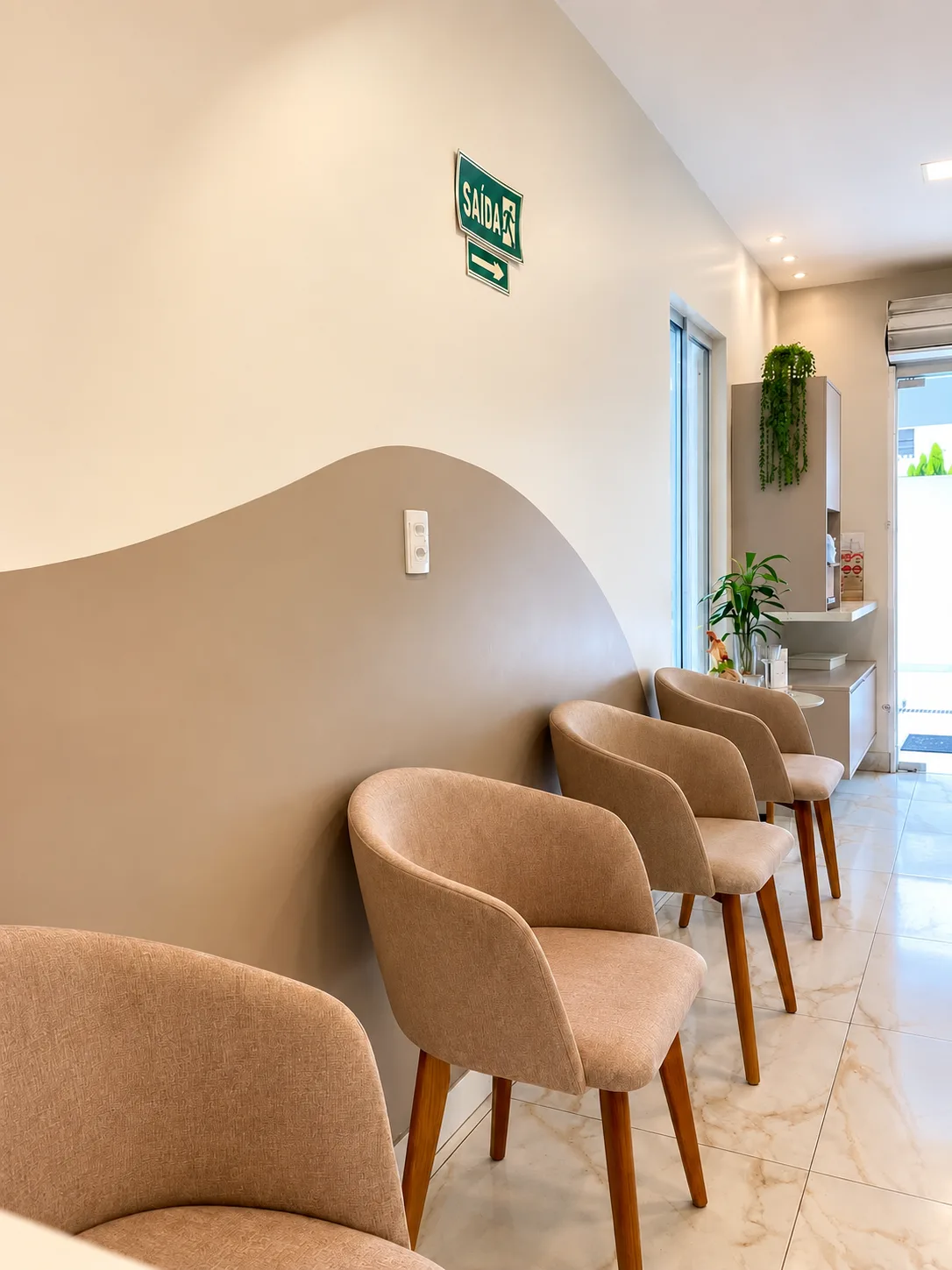 Sala de espera da Faccina com poltronas bege de pés de madeira, parede com onda pintada em bege e piso de mármore claro